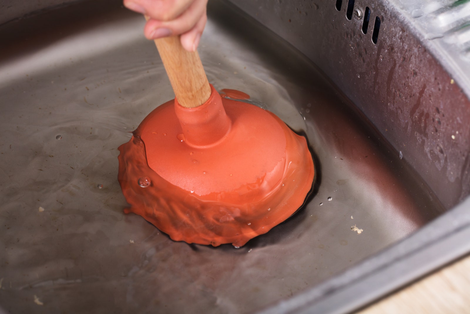 Closeup Of A Person Cleaning Sink Filled With Water With Cup Plunger